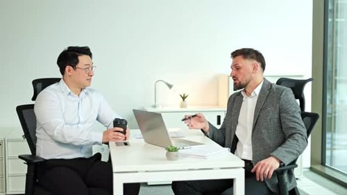 Businessmen in Office Meeting Discussing Work at Desk By Window