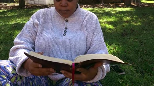 Medium close up of Black woman sitting reading bible and not paying attention to the distraction of