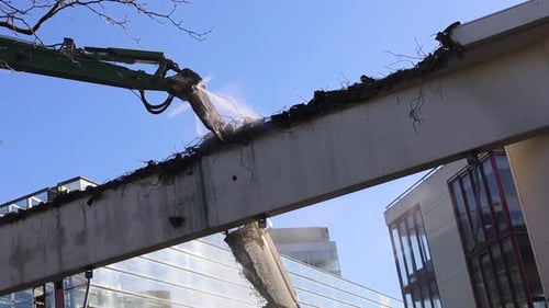 Une grue de démolition pulvérise de l'eau sur la pièce qu'elle démonte.