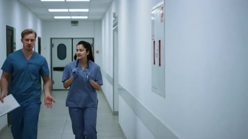 Two Doctors Walking Down Hospital Corridor Discussing Patient Diagnose. Young Physician Consultin...