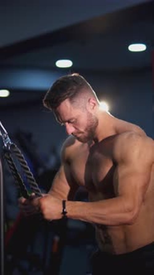 Athletic guy pumping his muscles. Shirtless bodybuilder training his sportive body in the gym.