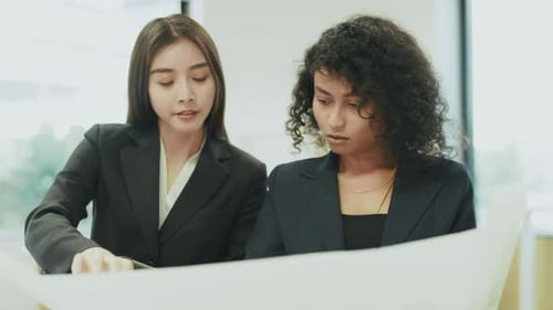 Two professional female architects analyzing blueprint