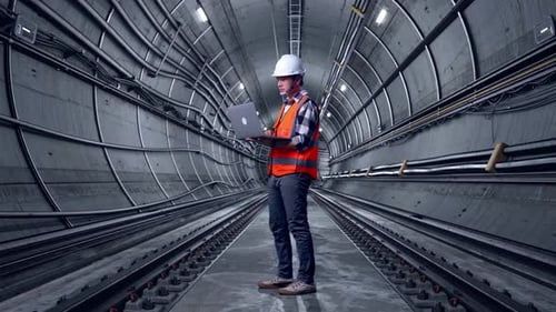 Full Body Side View Of Asian Male Engineer Working On A Laptop In Subway Tunnel
