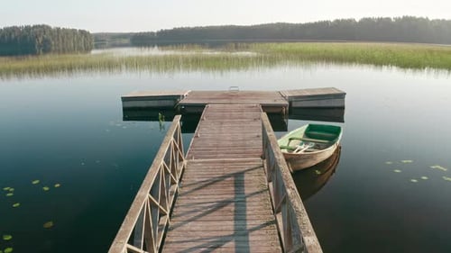 Drone Flies Over Wooden Old Boat Moored at Pier on Large Lake Among Forest