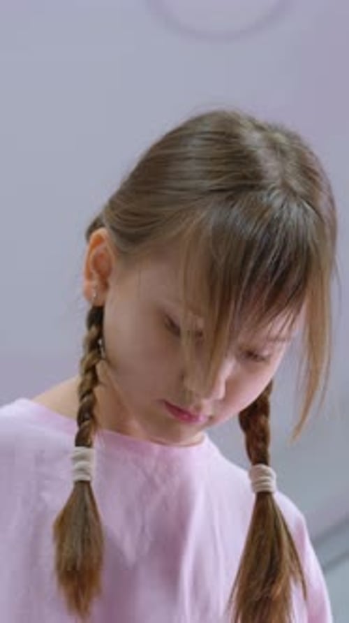 Young Child in Pink with Braids Looking Down in Focused Expression
