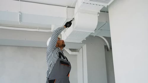 Tradesman Working on Ceiling Air Conditioning Unit
