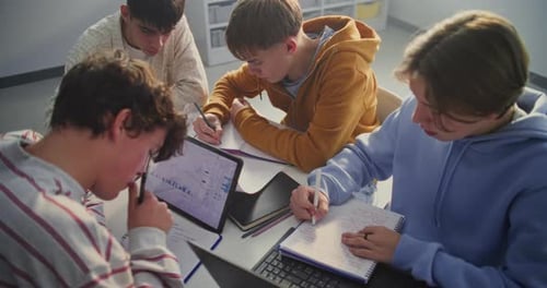 Four Young Students Gathers Around Table Intensely Focused on Collaborative Study Session