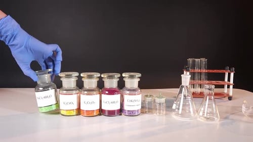La main d'une fille dans un gant en caoutchouc bleu place des bocaux en verre contenant des composés chimiques multicolores