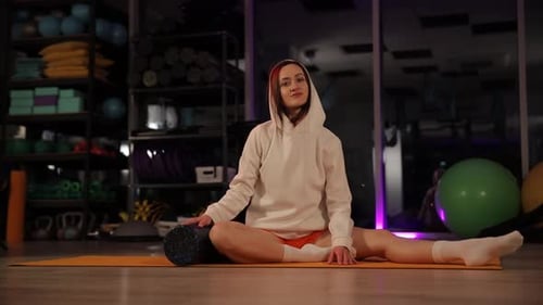 Woman Stretching Hamstrings with Foam Roller in Gym