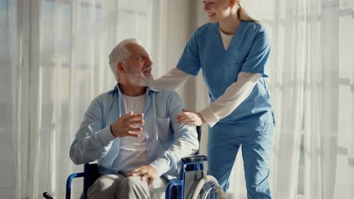 Senior Man in Wheelchair Conversing with Young Nurse