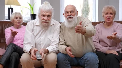 Concentrated Senior Men Talking Watching TV Ignoring Dissatisfied Women Sitting on Sofa Front View