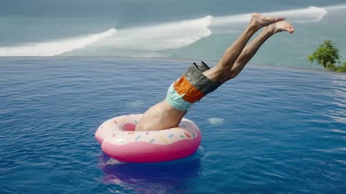 Man Jump in Inflatable Ring with Water Splash in Ocean View Infinity Pool