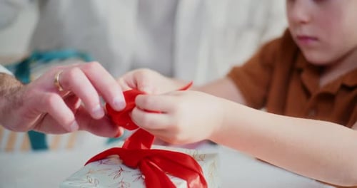 Child and Adult Untying Ribbon on Gift Together