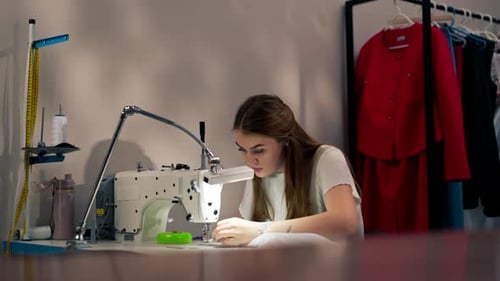 in the Sewing Workshop Young Girl Works with a Sewing Machine and White Fabric