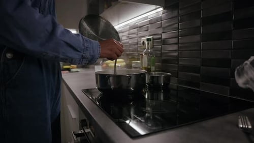 Girl holds the lid of a pot and checks the food on the stove using a fork, steaming hot boiling tast