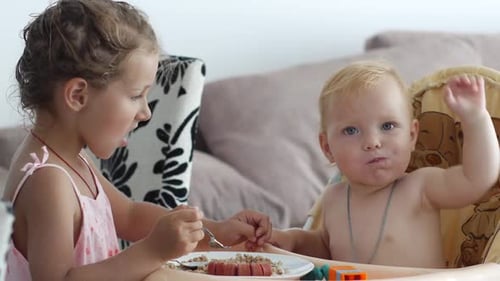 Child Feeds Baby in Highchair at Home