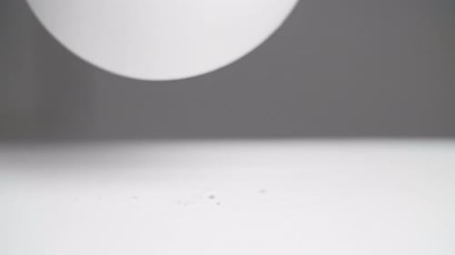 Close up: White plane sphere bouncing off a white surface with a dark background. Slow motion close