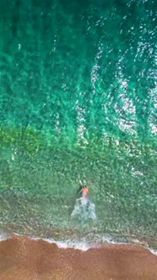 Aerial View of a Man in Red Shorts Swims in the Crystal Clear Sea Water