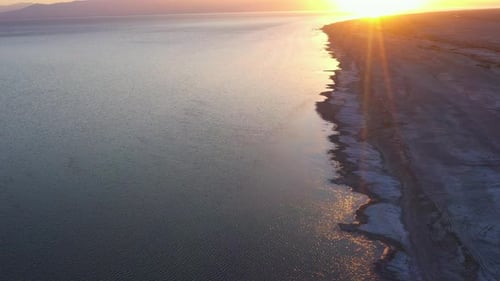 Sensational seaside flight above desert shoreline towards bright white sun and yellow sunset at dusk