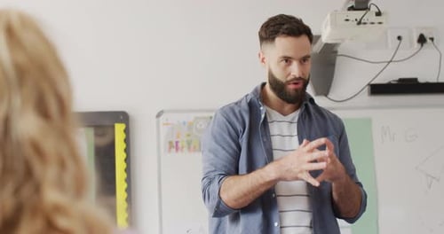 Diverse male teacher and schoolchildren at desks in school classroom