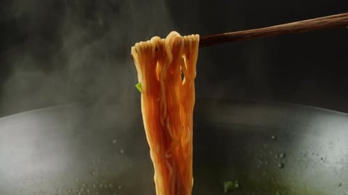 Steamy Noodles Held Up by Chopsticks in Kitchen
