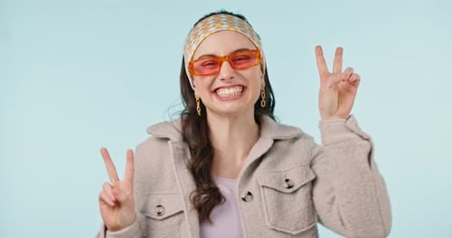 Fashion, face and woman with peace sign for happiness, aesthetic and trendy outfit in studio on blue