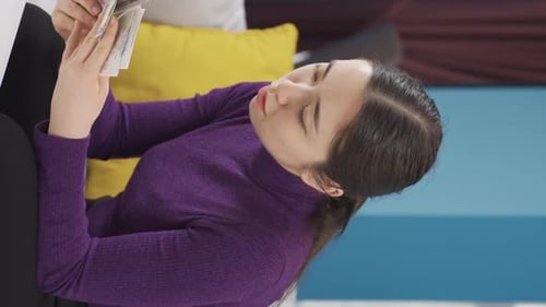 Vídeo vertical de una mujer asiática mirando sus facturas, después de calcularlas, mira su dinero.