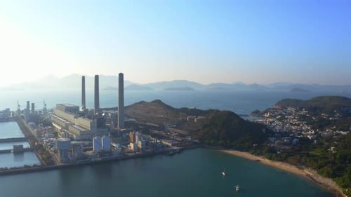 Drone shot of a big coastal coal-fired power plant on an island next to a village with a beach durin