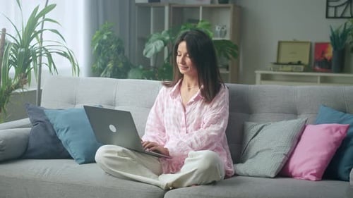 Stylish woman working on laptop in cozy home office with plants