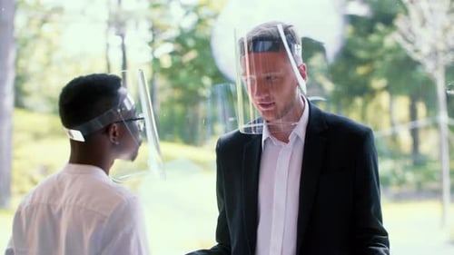 Two Happy Young Male Multiethnic Business Partners Talking at Modern Office Window Wearing COVID19