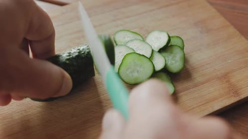 Slicing Fresh Cucumber on Wooden Cutting Board