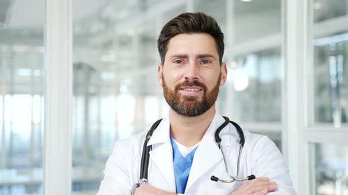 Portrait of smiling handsome doctor in white coat standing in modern hospital clinic looking