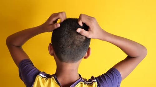 Boy Scratches Head in Front of Yellow Backdrop