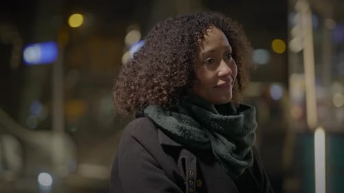 Woman Outdoors at Night Calm in City in Warm Coat and Scarf Under Urban Lights
