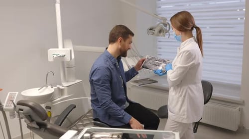 Young attractive man visiting dentist, sitting in dental chair at modern light clinic