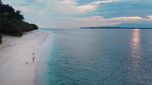 Beautiful woman walking on sandy beach and turquoise sea at dawn. Waves lapping to her feet during s