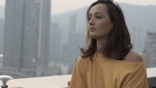 Worried young woman checks phone impatiently waiting at rooftop bar in city night