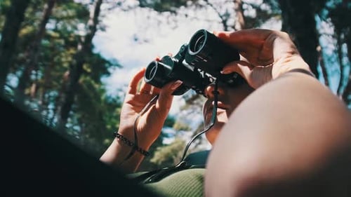 Femme regarde à travers des jumelles sur une chaise longue dans une forêt près du camping