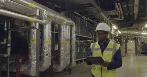 Afroamerikanischer männlicher Ingenieur inspiziert einen industriellen Anlagenraum
