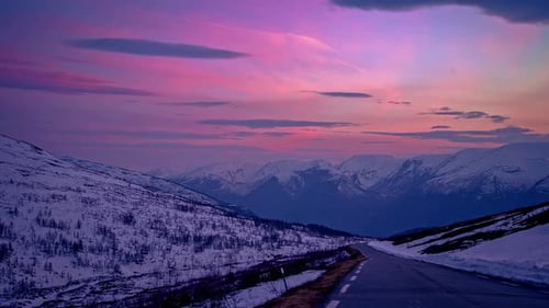 Static shot of winding road through winter mountains during evening time in timelapse.