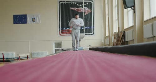 Niedriger Winkel eines jungen männlichen Turners in Sportbekleidung, der Sprünge macht, während er alleine im geräumigen Raum trainiert