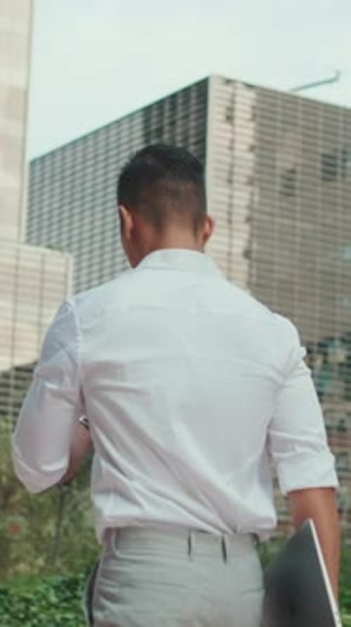 Young businessman is walking on modern building background. Back view