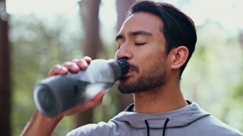 Health, fitness and man drinking water in a park resting, thirsty and tired from training