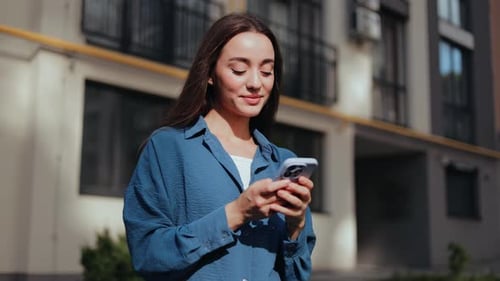 Smiling Young Woman Using Phone On Sunny City Street