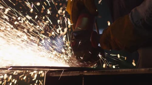 Heavy industry worker at a factory is working with metal on a angle grinder while hot sparks are pr