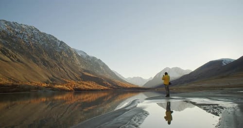 Man Taking Photo with Smartphone By Mountain Lake at Sunrise