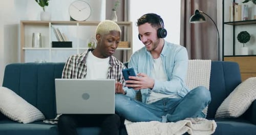 Two Men Using Phone and Laptop on Couch