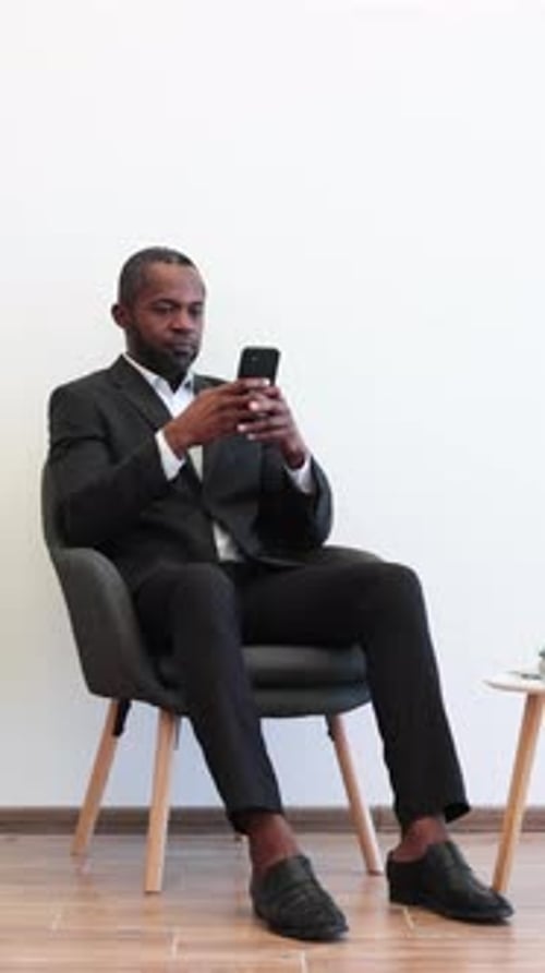 Man in Suit Sits, Looks at Mobile Phone