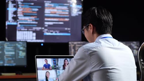 Male Programmer Having A Meeting By A Laptop While Writing Code On Multiple Monitors