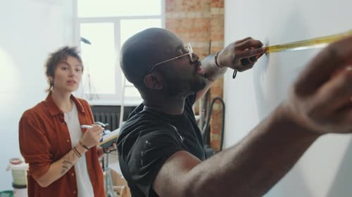 Husband Measuring Wall as Wife Taking Notes during Home Remodeling